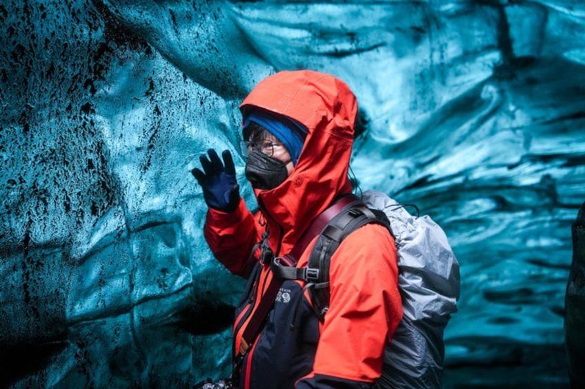 A person in a red jacket and blue helmet standing in front of a glacier. 5