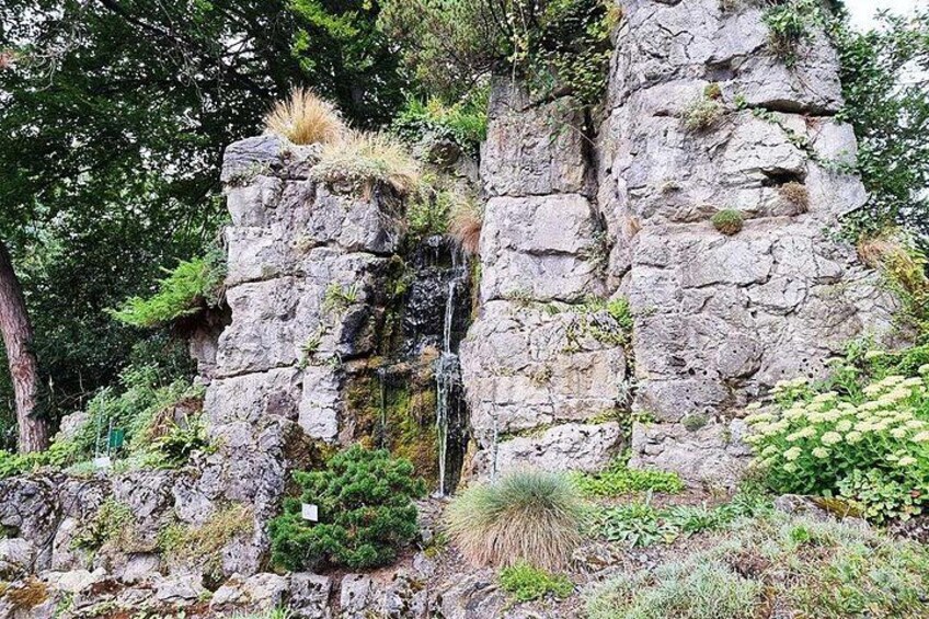 A rocky cliff with a small waterfall, surrounded by greenery and trees. 2