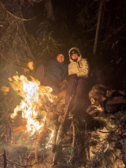 Two people sitting by a campfire in a forest. 2