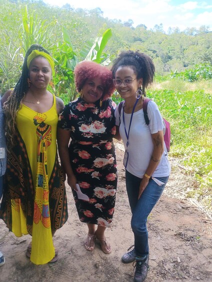 Three people standing on a dirt path with greenery in the background. 4