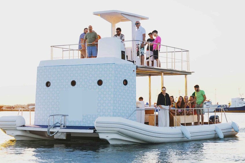 A multi-deck boat with people on the upper deck and a dining area on the lower deck. 1