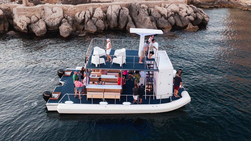 A boat with people on deck, a covered seating area, and a rocky shoreline in the background. 2
