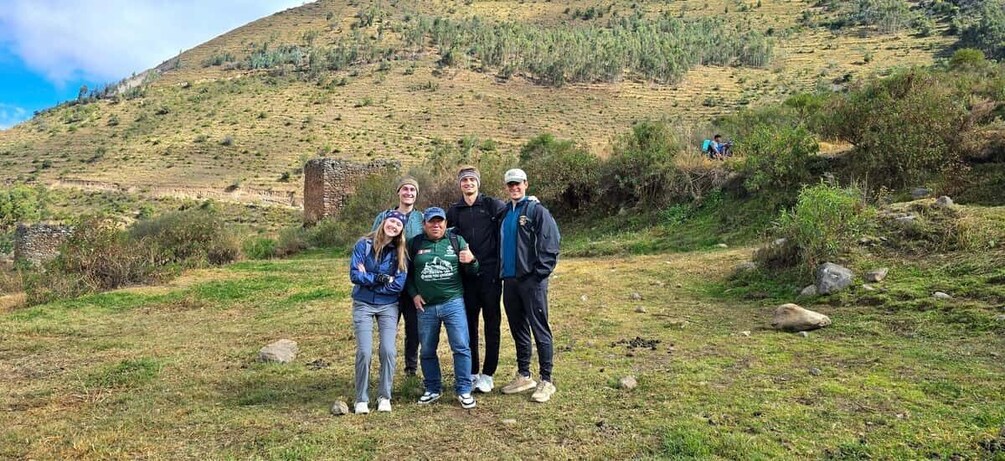 A group of people standing on a grassy hill with a stone structure in the background. 3