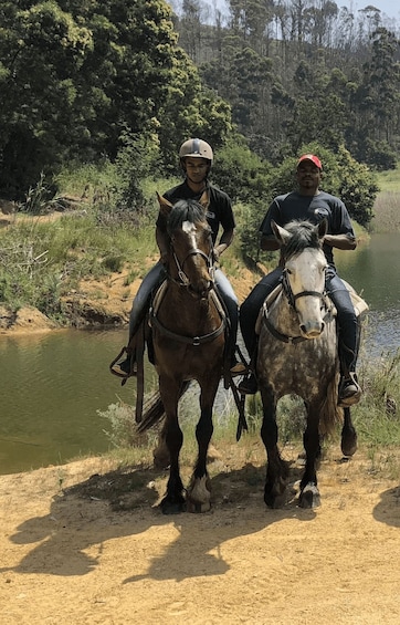 Two people riding horses along a riverbank. 1