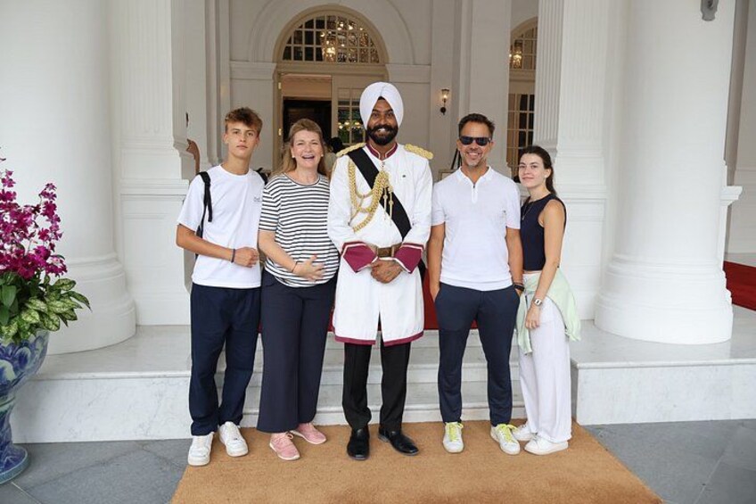 A group of people standing on a carpeted area in front of a building with white columns and a large door. 5