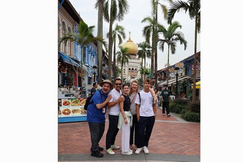 A group of people standing on a brick-paved street with palm trees and a building with a golden dome in the background. 3