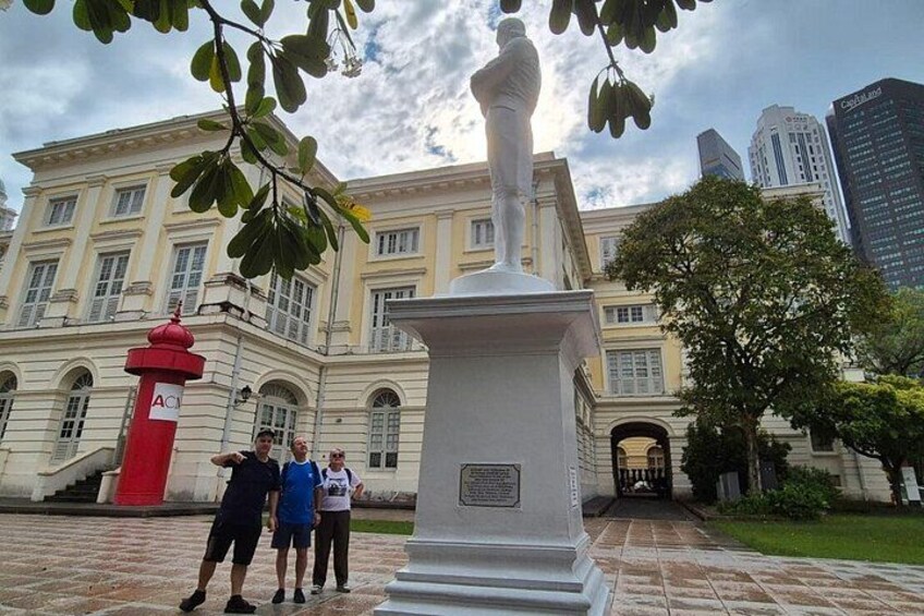 A statue in front of a building with a red postbox and a tree in the foreground. 4