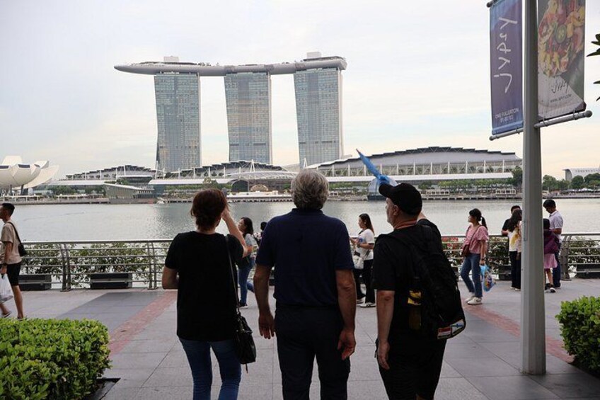 People walking along a waterfront promenade with a view of the Marina Bay Sands hotel. 2