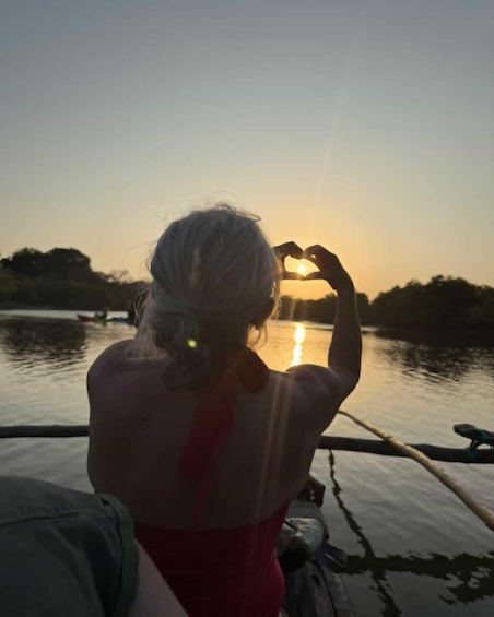 A person making a heart shape with their hands, facing a sunset over water. 3
