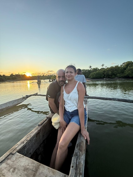 Two people in a wooden boat on a calm body of water with a sunset in the background. 2