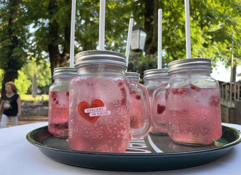 Mason jars with heart-shaped labels filled with pink beverages, placed on a tray outdoors. 2