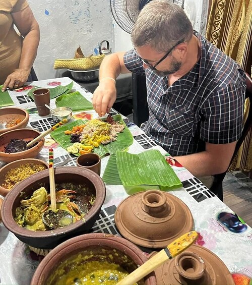 A person sitting at a table with various dishes, including seafood and vegetables, served on banana leaves. 2
