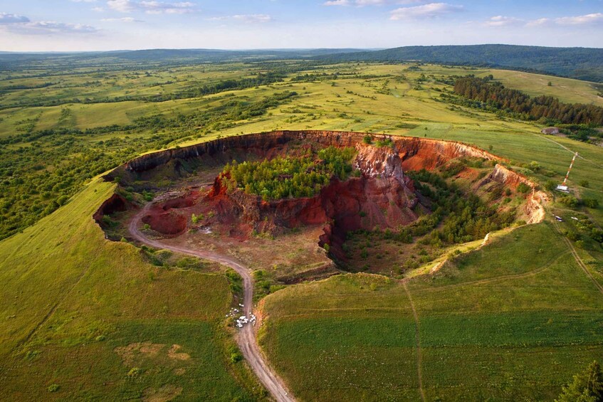 An aerial view of a large, circular geological formation surrounded by green fields and a winding road. 2