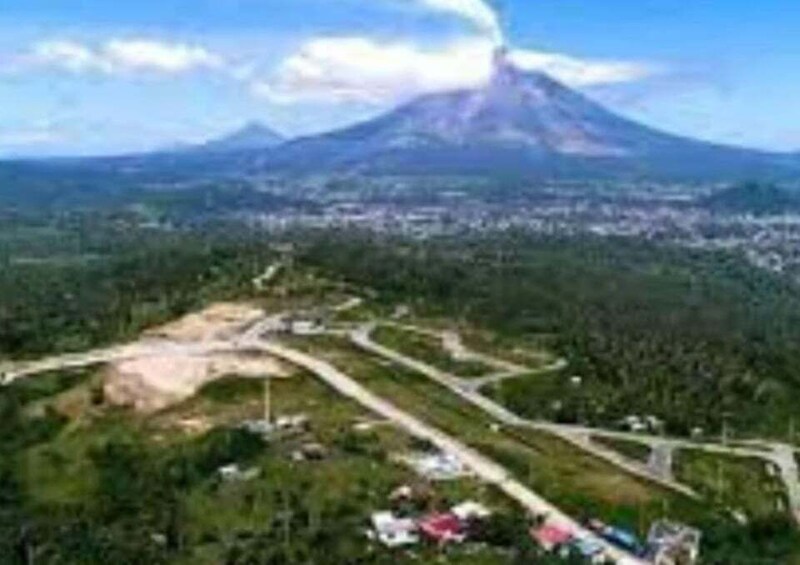 A volcano with a clear sky, a road winding through a green area, and a distant town. 3