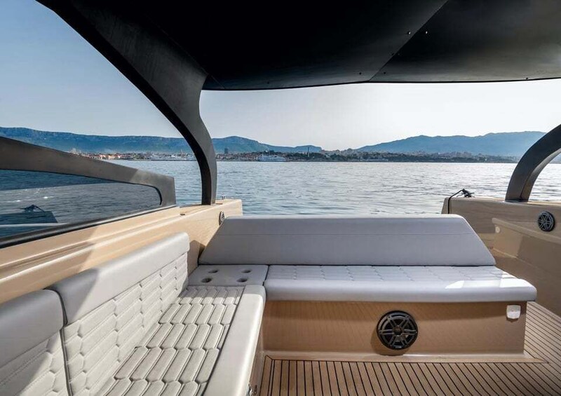 A boat's interior with a cushioned seating area and a view of a calm body of water and distant hills. 2