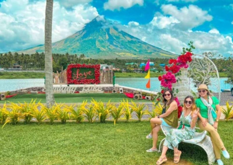 A group of people sitting on a bench with a backdrop of a lake, a mountain, and a sign that says 'Love'. 3