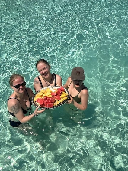 Three people holding a tray of fruit in clear water. 3