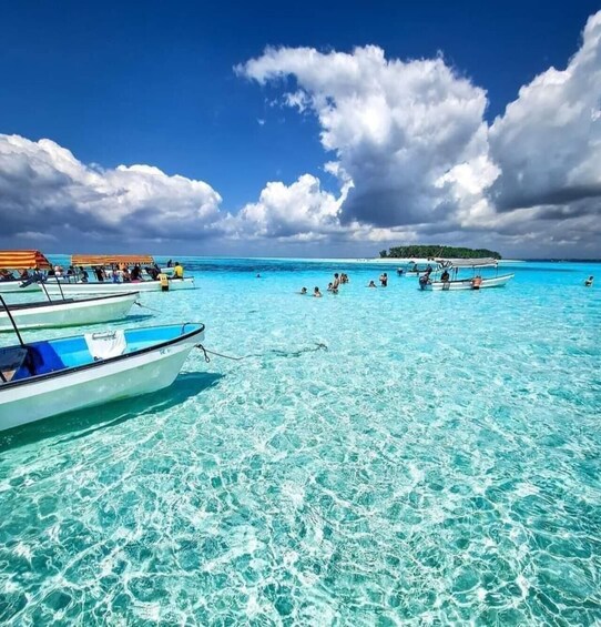A clear turquoise sea with boats and people in the water. 1