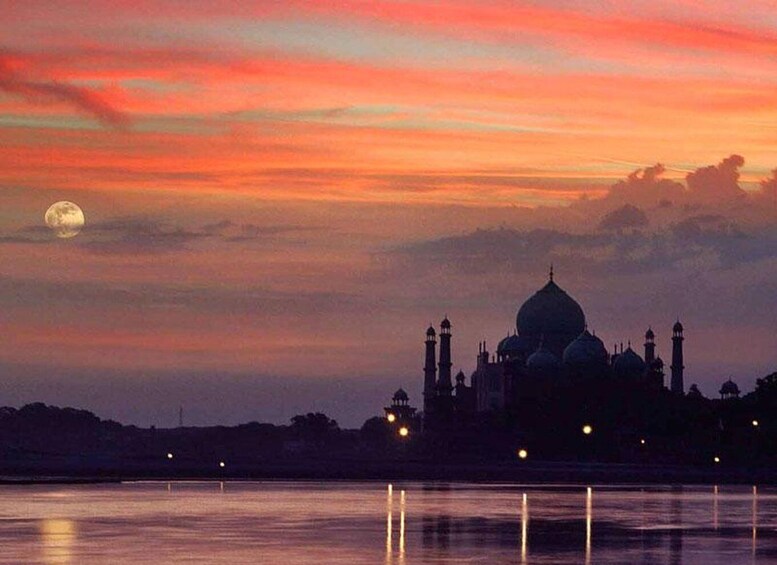 The Taj Mahal at dusk with a moon in the sky and a reflection on the water. 4