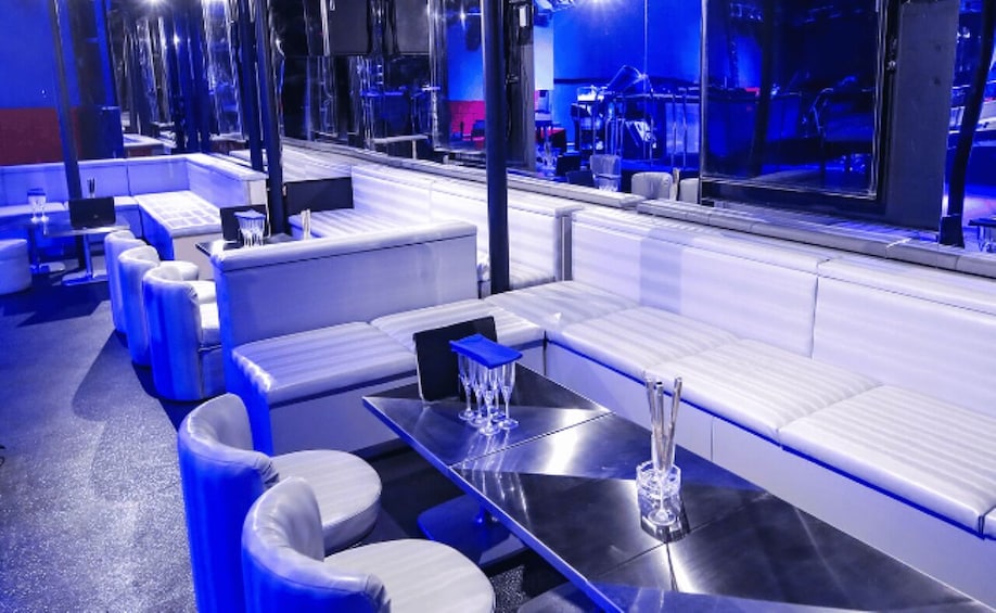A modern lounge with white sofas, a glass table, and blue ambient lighting. 4