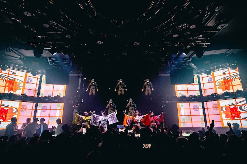 A stage performance with performers in traditional attire, a large audience, and a backdrop with geometric patterns. 5