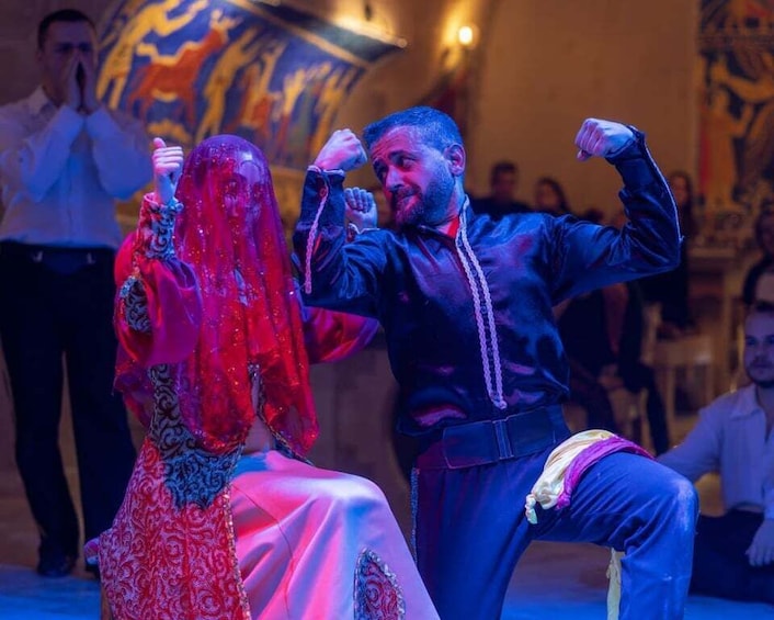 A person in a red dress and another in a dark jacket dancing on a stage with a crowd in the background. 4