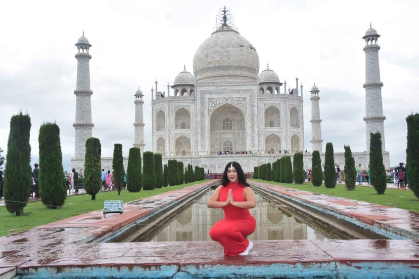 A person in a red dress posing in front of the Taj Mahal with its reflection in the water. 5