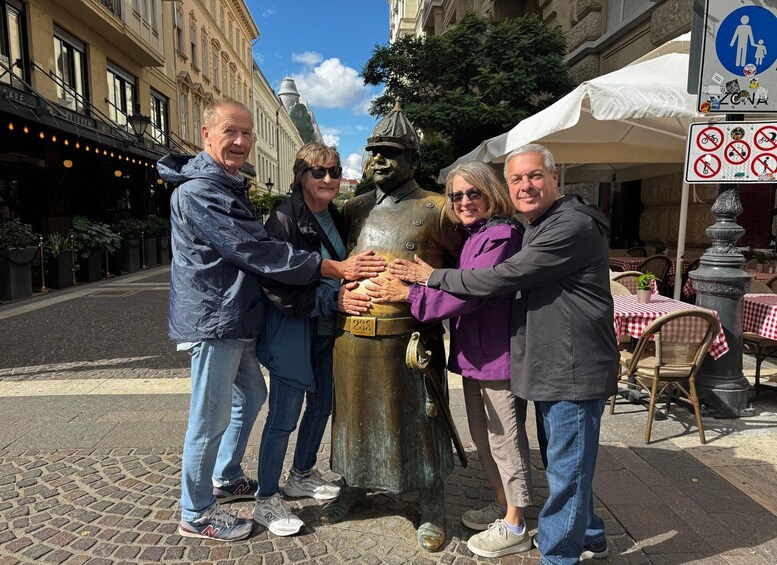 A group of people standing around a bronze statue on a cobblestone street with buildings and outdoor seating in the background. 5