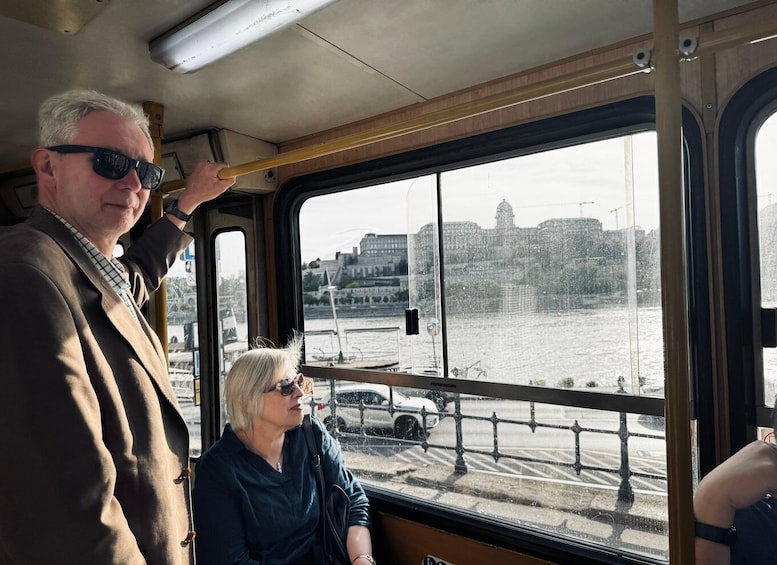 A bus interior with passengers looking out at a river and buildings in the background. 1