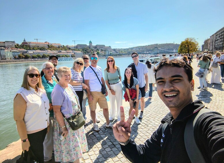 A group of people standing on a riverside promenade with a bridge in the background. 4