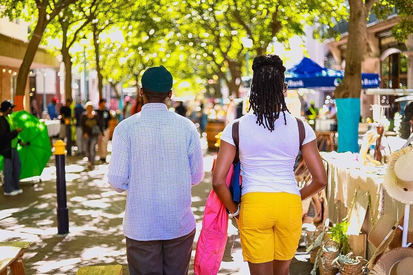 A couple walking down a tree-lined street with market stalls. 3
