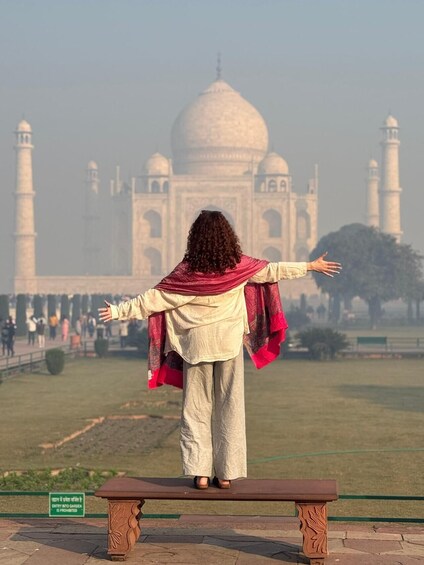 A person standing on a bench with arms outstretched, facing the Taj Mahal. 3