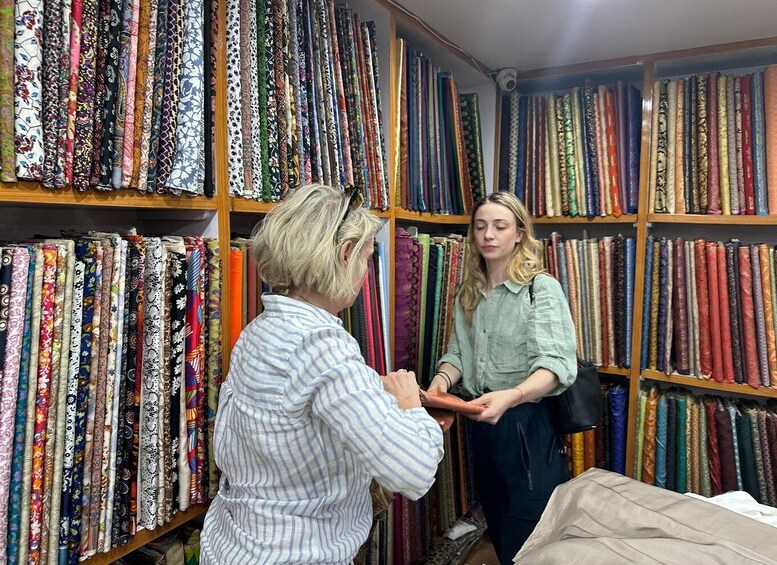 Two people in a fabric store surrounded by shelves of colorful fabrics. 1