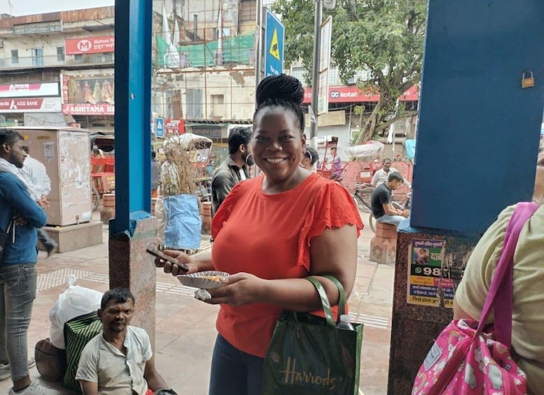 A woman holding a tray with food, standing in a busy street with shops and people in the background. 4