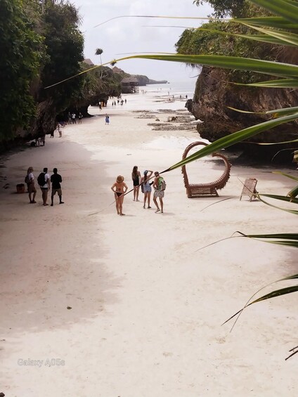 A beach with people walking, a large rock formation, and a circular structure. 4