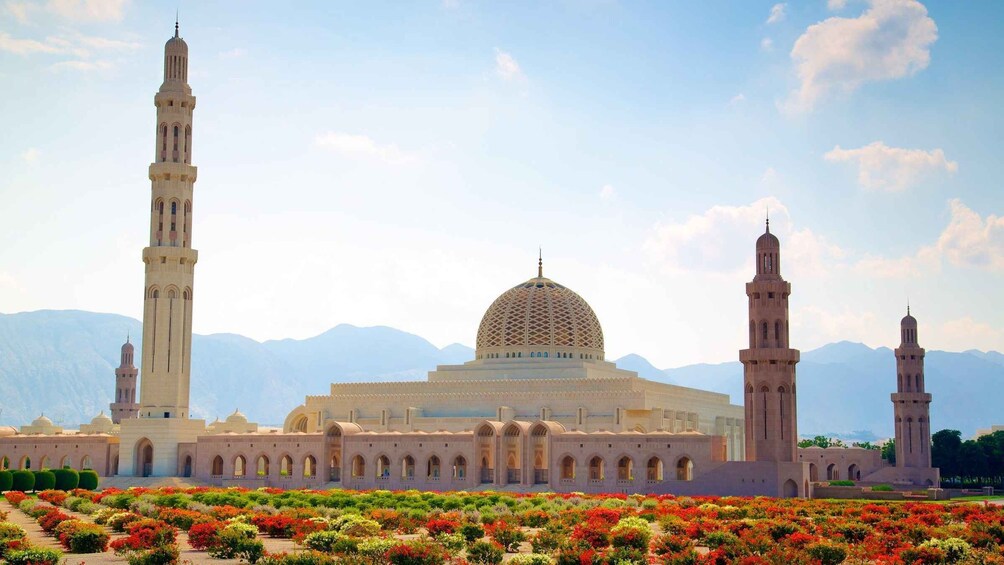 Una mezquita con dos minaretes y una gran cúpula, rodeada de jardines coloridos y montañas al fondo. 1