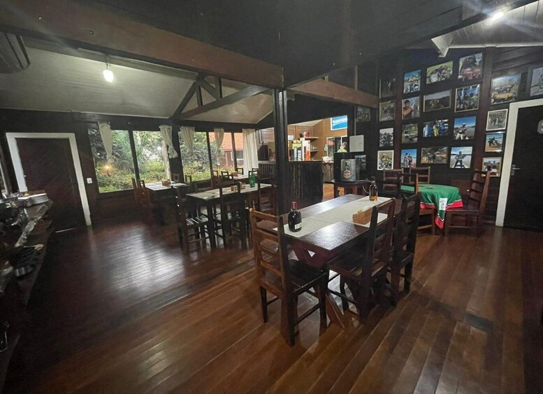 A spacious dining area with wooden tables and chairs, a kitchen in the background, and a wall decorated with framed pictures. 4
