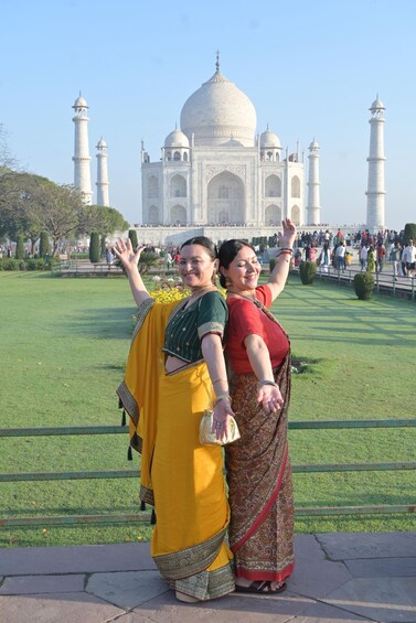 Kaksi naista perinteisissä asuissa poseeraavat Taj Mahalin edessä. 3