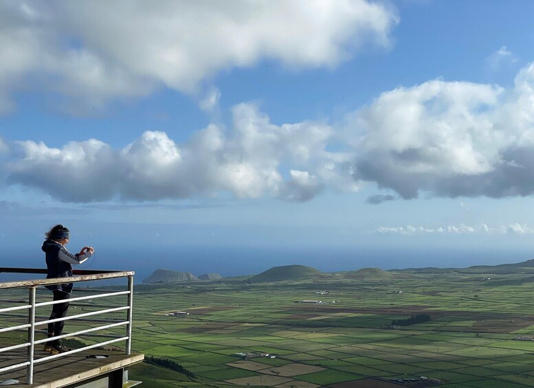A person standing on a platform overlooking a landscape of green fields and distant hills under a partly cloudy sky. 2
