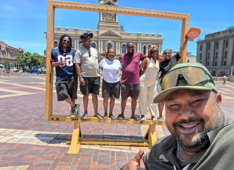 A group of people posing in front of a yellow frame with a cityscape in the background. 5