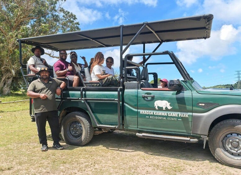 A green safari vehicle with passengers, parked on a grassy field with trees in the background. 2