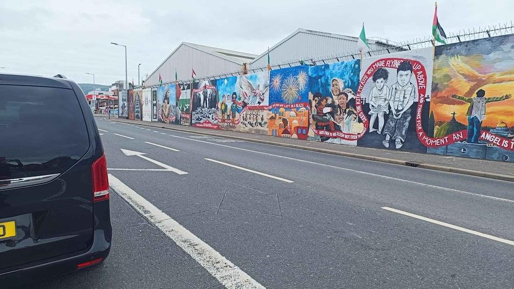 A road with a mural on the side depicting various scenes and figures. 3