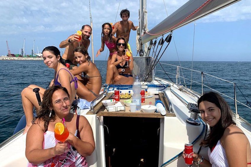 Un grupo de personas en un velero con vistas despejadas al mar y estructuras industriales a lo lejos. 3