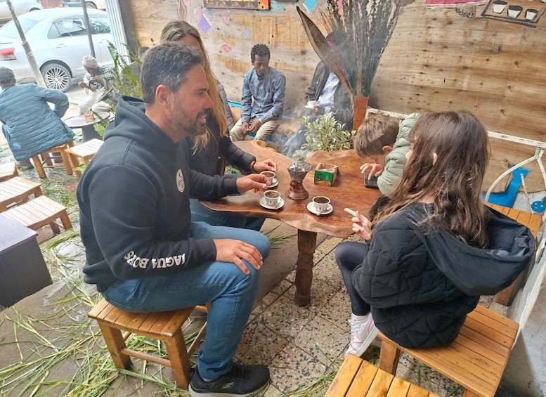 A group of people sitting at a wooden table outdoors, engaged in conversation. 5