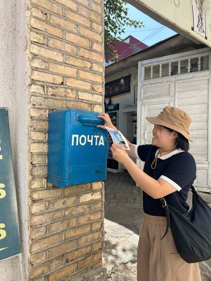 A person interacting with a blue mailbox labeled 'ПОЧТА' on a brick wall. 4