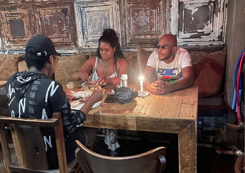 Three people dining at a wooden table in a rustic setting with peeling walls. 3