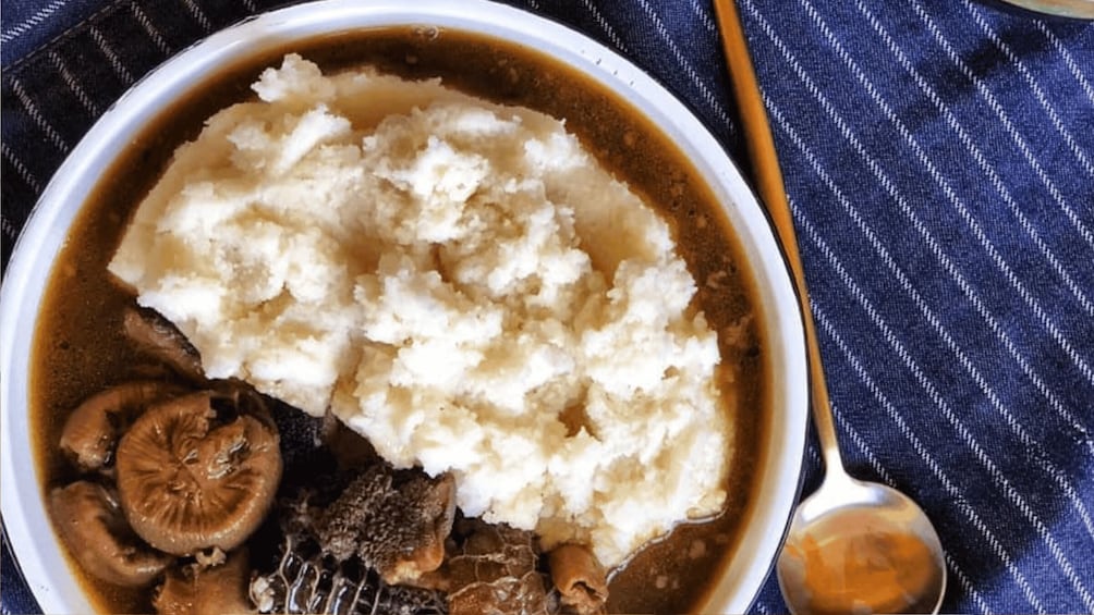 A bowl of mashed potatoes with gravy and mushrooms. 1