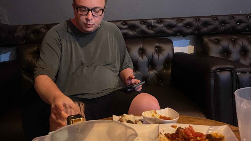 A person sitting on a leather couch with a smartphone, a glass, and a bowl of food on a table. 2