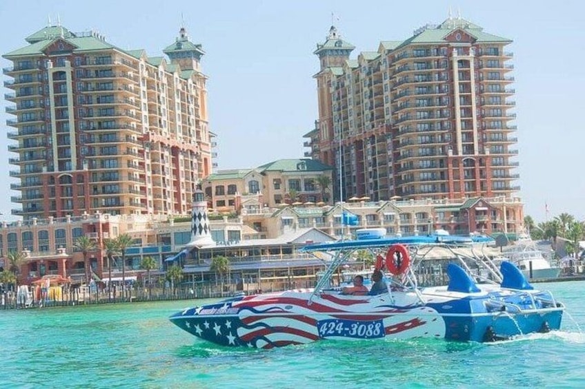 A speedboat with American flag design on the water, a marina with yachts, and two large hotel buildings in the background. 4