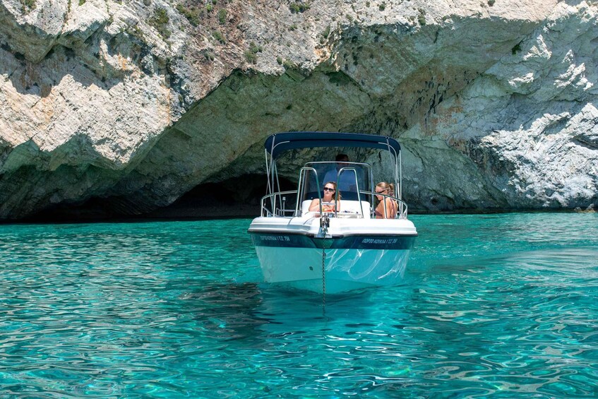 A boat with passengers on clear turquoise water near a rocky cave. 2